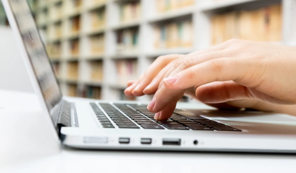 Hands typing on laptop in library