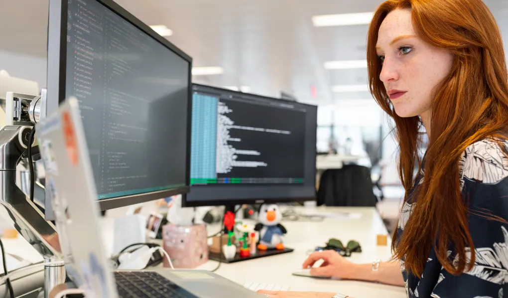 Young woman working on multiple screens at her desk