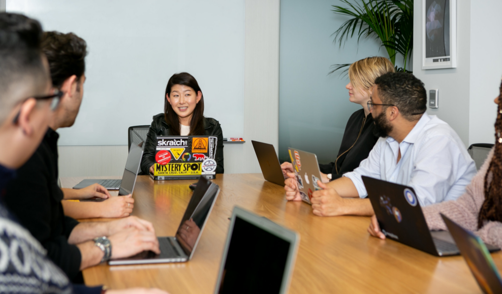 Female leader sitting in a meeting, group of four looking at her with laptops in front of them