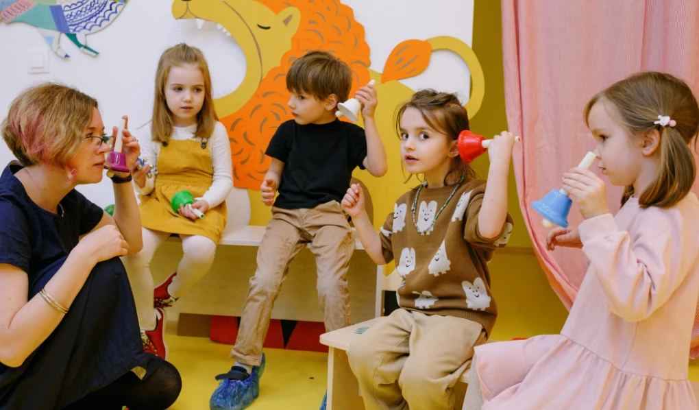 Kindergarten teacher with four kids holding small bells