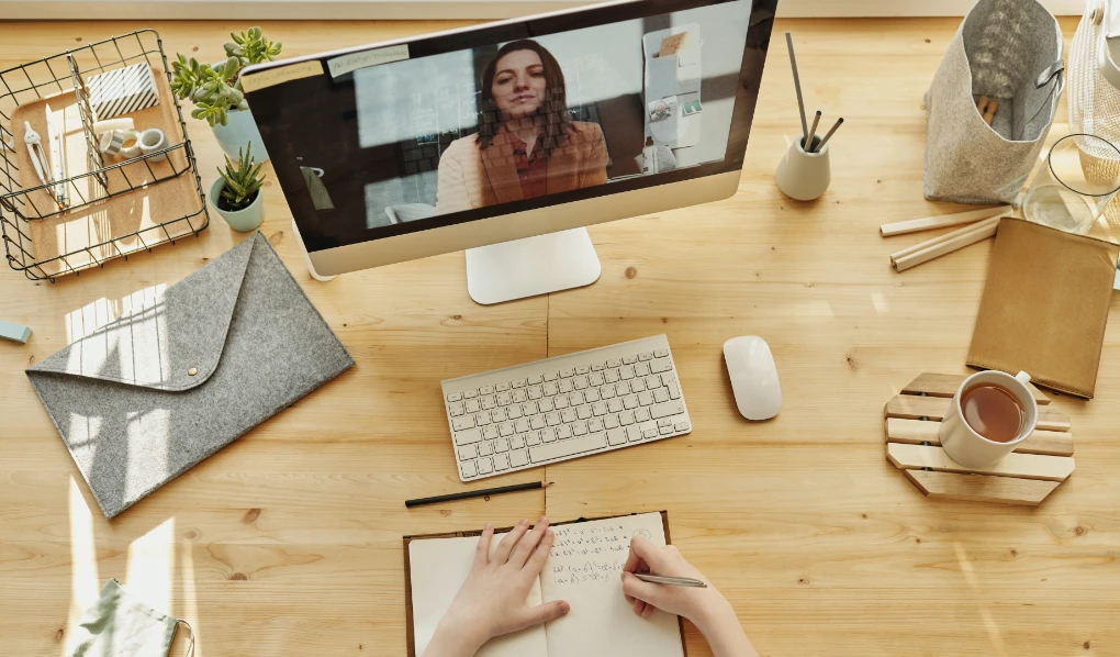 Study station with laptop, coffee, plants and hands making notes while on video call