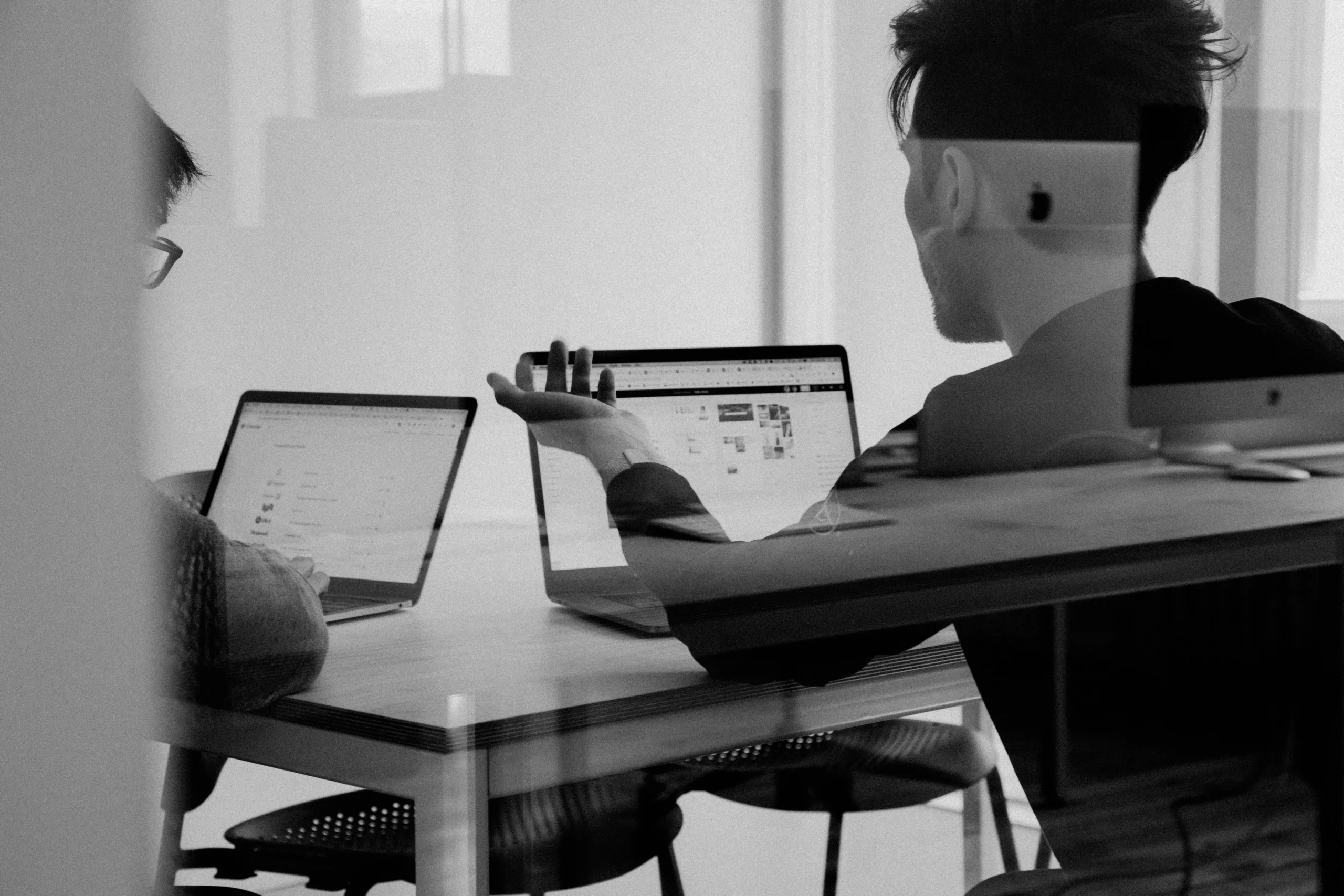 Two young men discussing work while working on their laptops