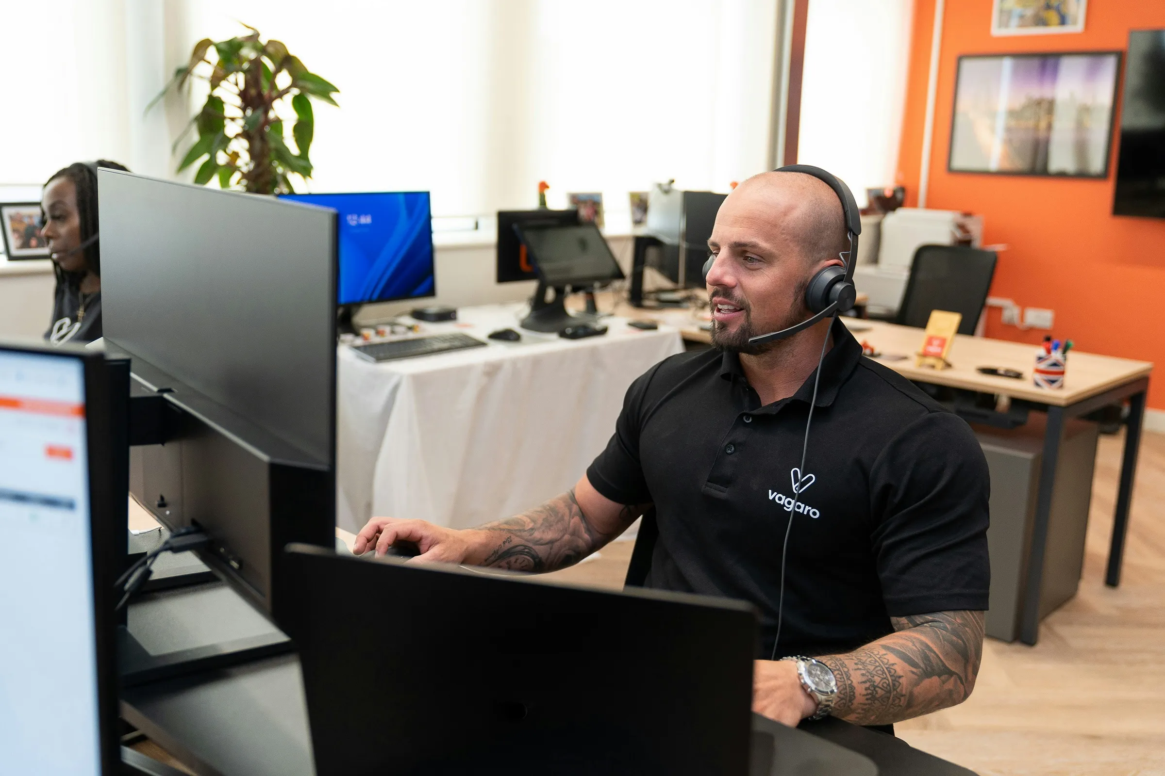 Tattooed man working on multiple screen while on a call via a headset