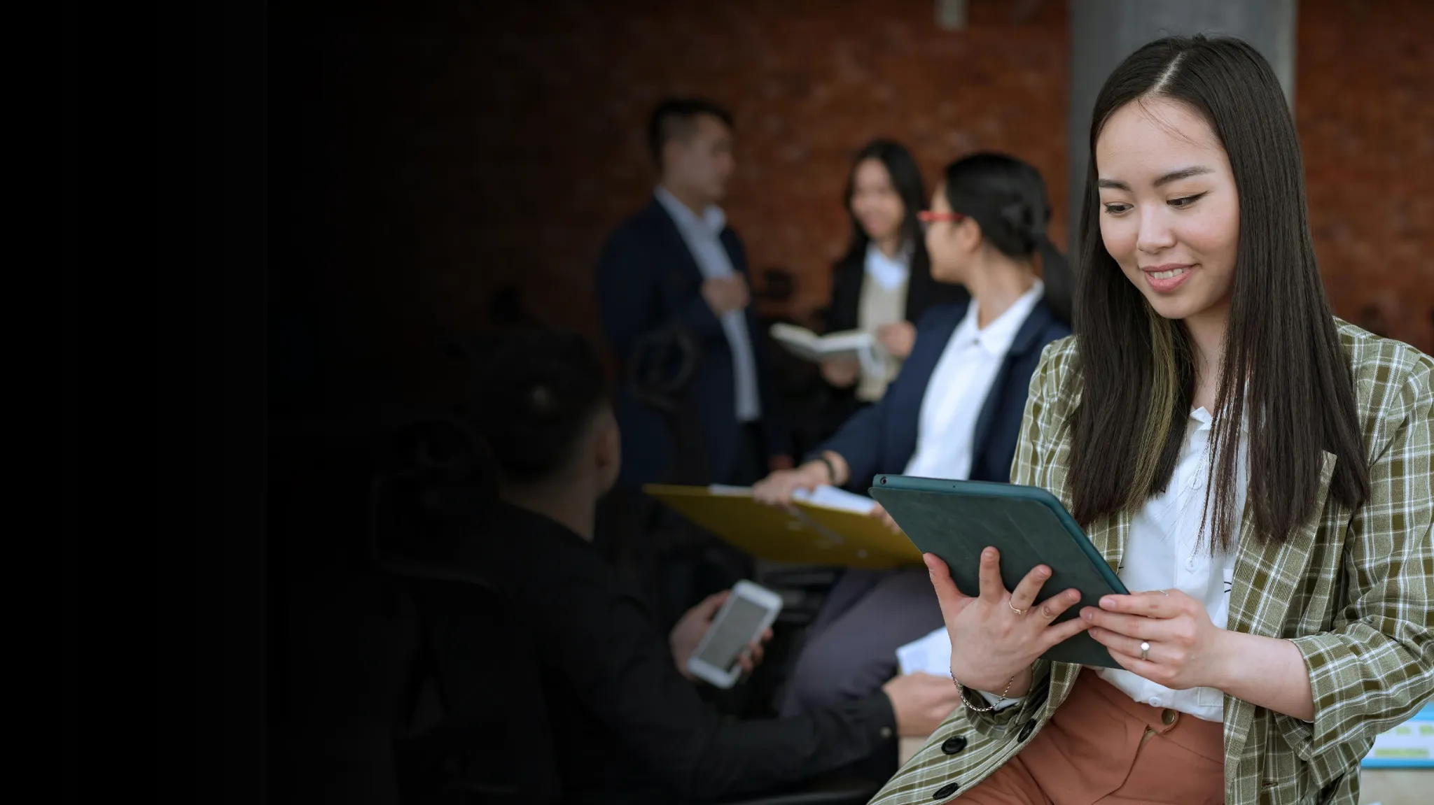 Young Asian woman reading on a tablet, while sitting with a group
