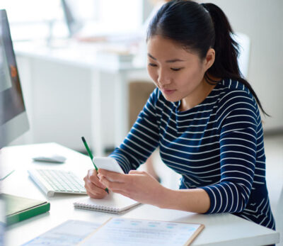 Young woman making notes while looking at her phone