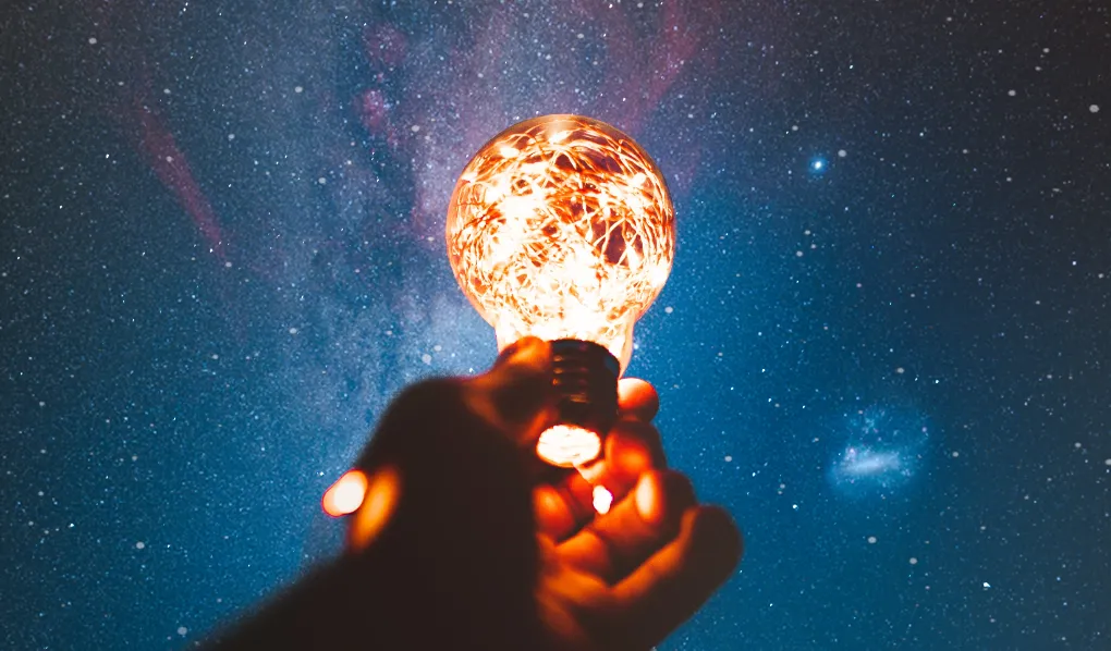 Lightbulb being held up to night sky