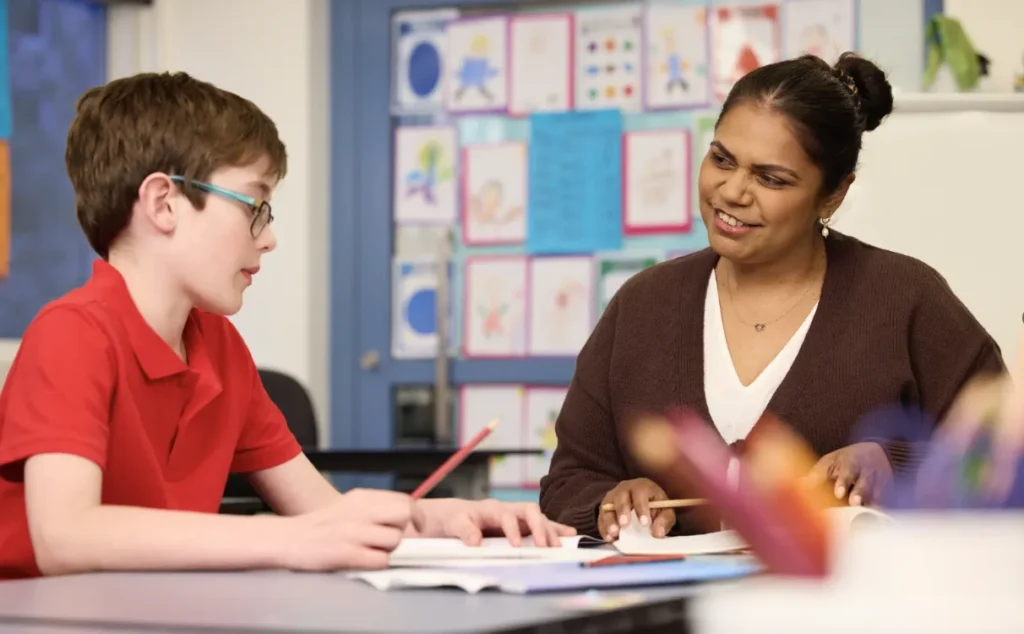 What skills do primary teachers need for today’s diverse classrooms - primary teacher engaging with a young student at a desk